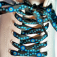 Close-up of a shoe with black and blue evil eye patterned shoelaces on a white background