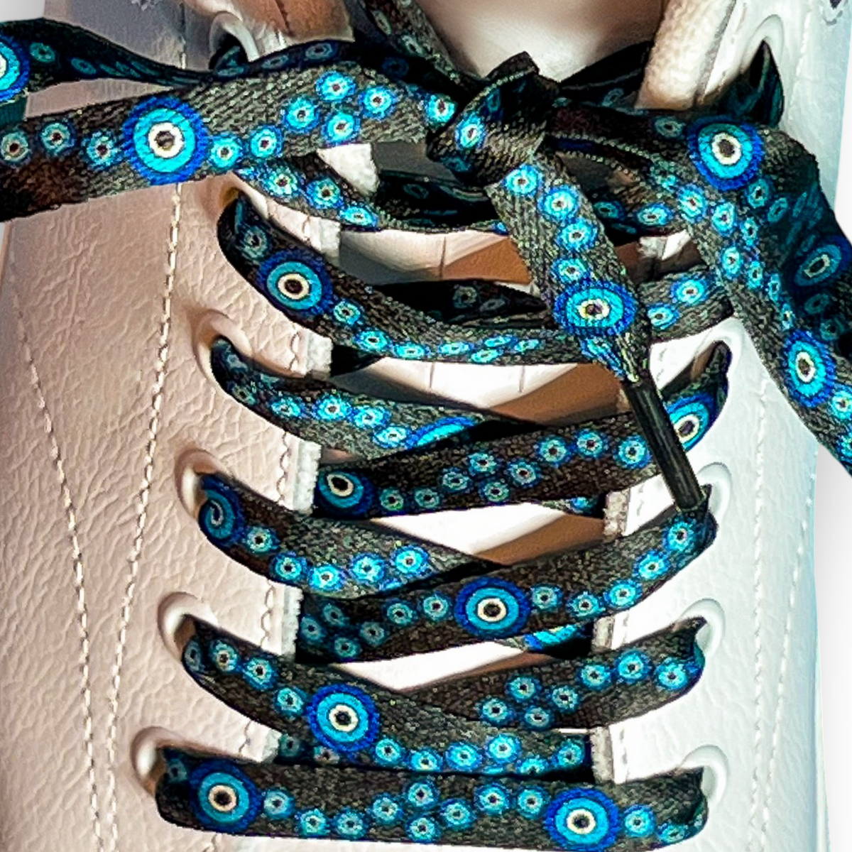 Close-up of a shoe with black and blue evil eye patterned shoelaces on a white background
