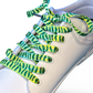 White sneaker with green and yellow pickle laces on a white background