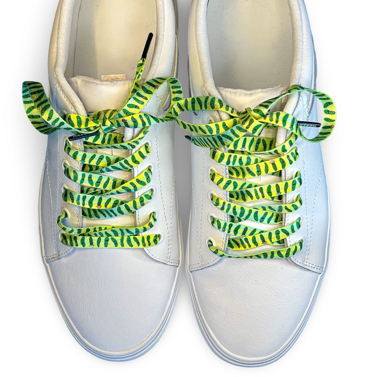 White sneakers with Green and yellow pickle patterned shoelaces on a white background