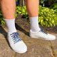 White sneakers with colorful retro laces worn on a concrete surface with greenery in the background