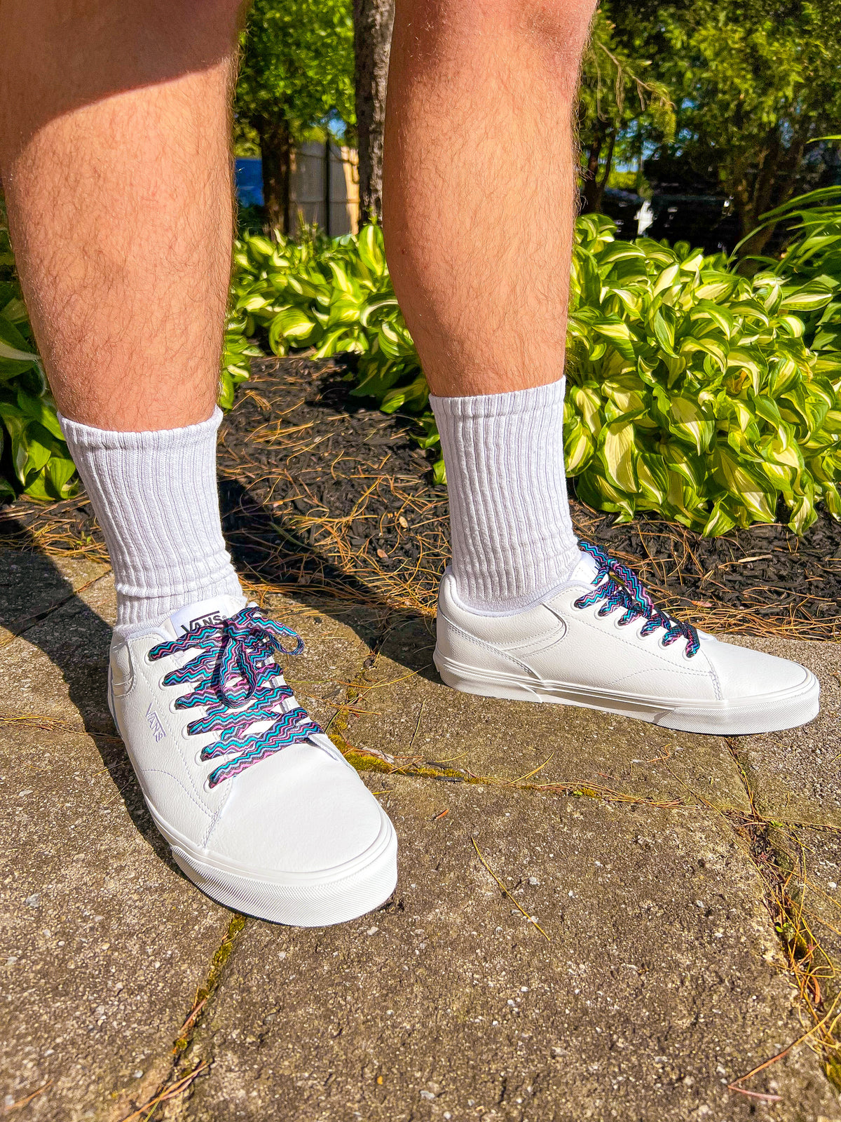 White sneakers with colorful retro laces worn on a concrete surface with greenery in the background