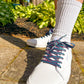 White sneakers with colorful retro laces worn outdoors on a concrete surface.