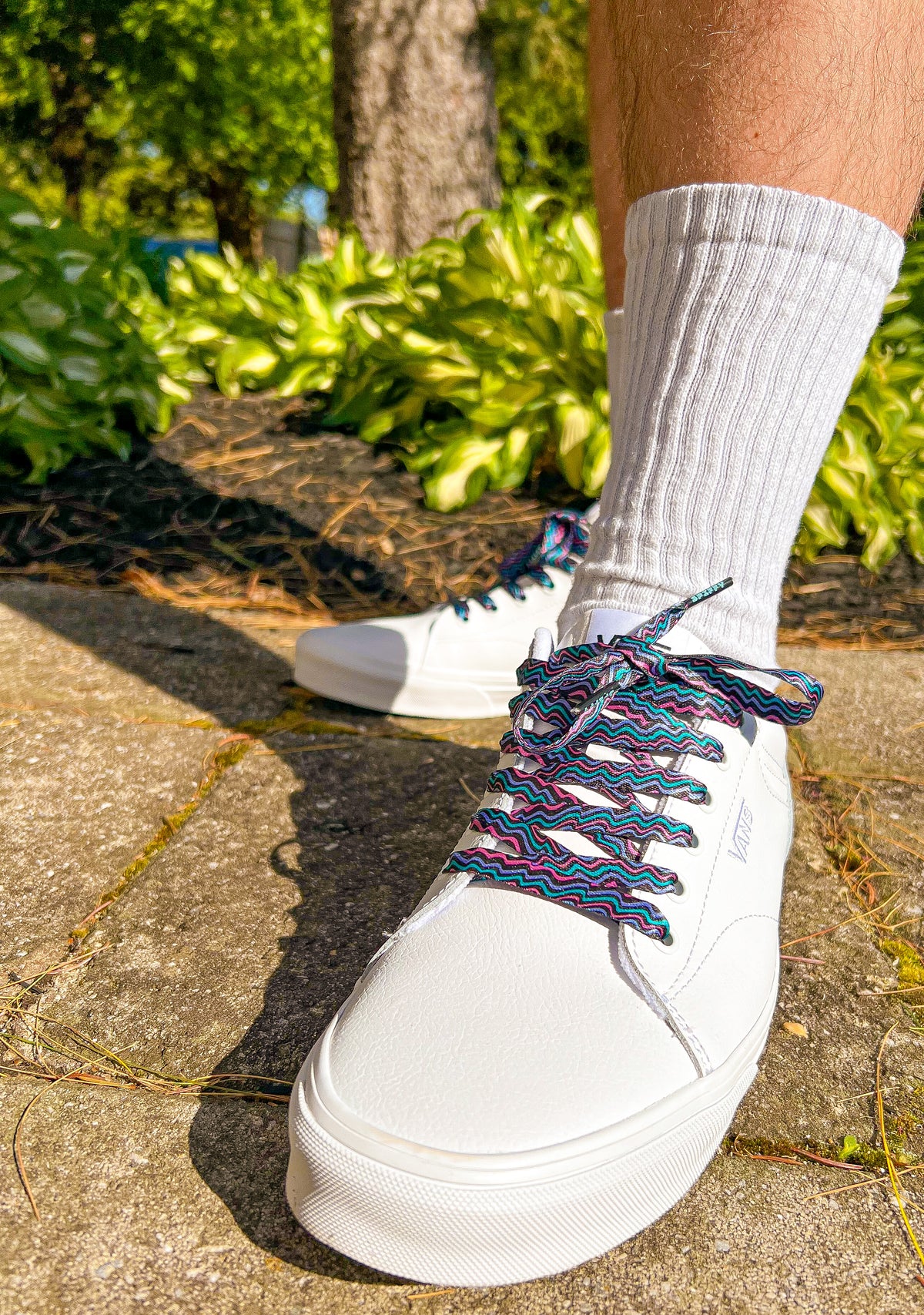 White sneakers with colorful retro laces worn outdoors on a concrete surface.
