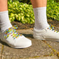 White sneakers with colorful laces worn on a concrete surface with greenery in the background