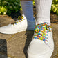 White sneakers with colorful laces worn on a concrete surface with greenery in the background