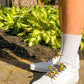 White sneakers with colorful wizards on a person standing on a sidewalk next to green plants.