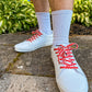 White sneakers with colorful heart shoelaces worn on a concrete surface with greenery in the background