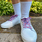 White sneakers with colorful and fun lobster shoelaces worn on a concrete surface with greenery in the background