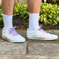 White sneakers with colorful and fun lobster shoelaces worn on a concrete surface with green plants in the background