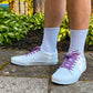 White sneakers with colorful and fun lobster shoelaces worn on a concrete surface with greenery in the background