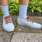 White sneakers with tapestry designed laces worn by a person on a concrete surface with greenery in the background