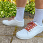 White sneakers with colorful laces worn on a concrete surface with greenery in the background