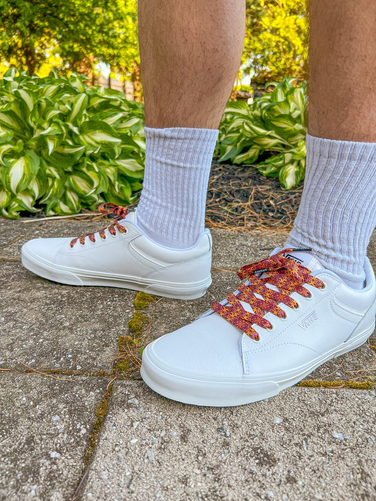 White sneakers with colorful laces worn on a concrete surface with greenery in the background