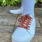 White sneakers with orange and red patterned laces on a concrete surface.