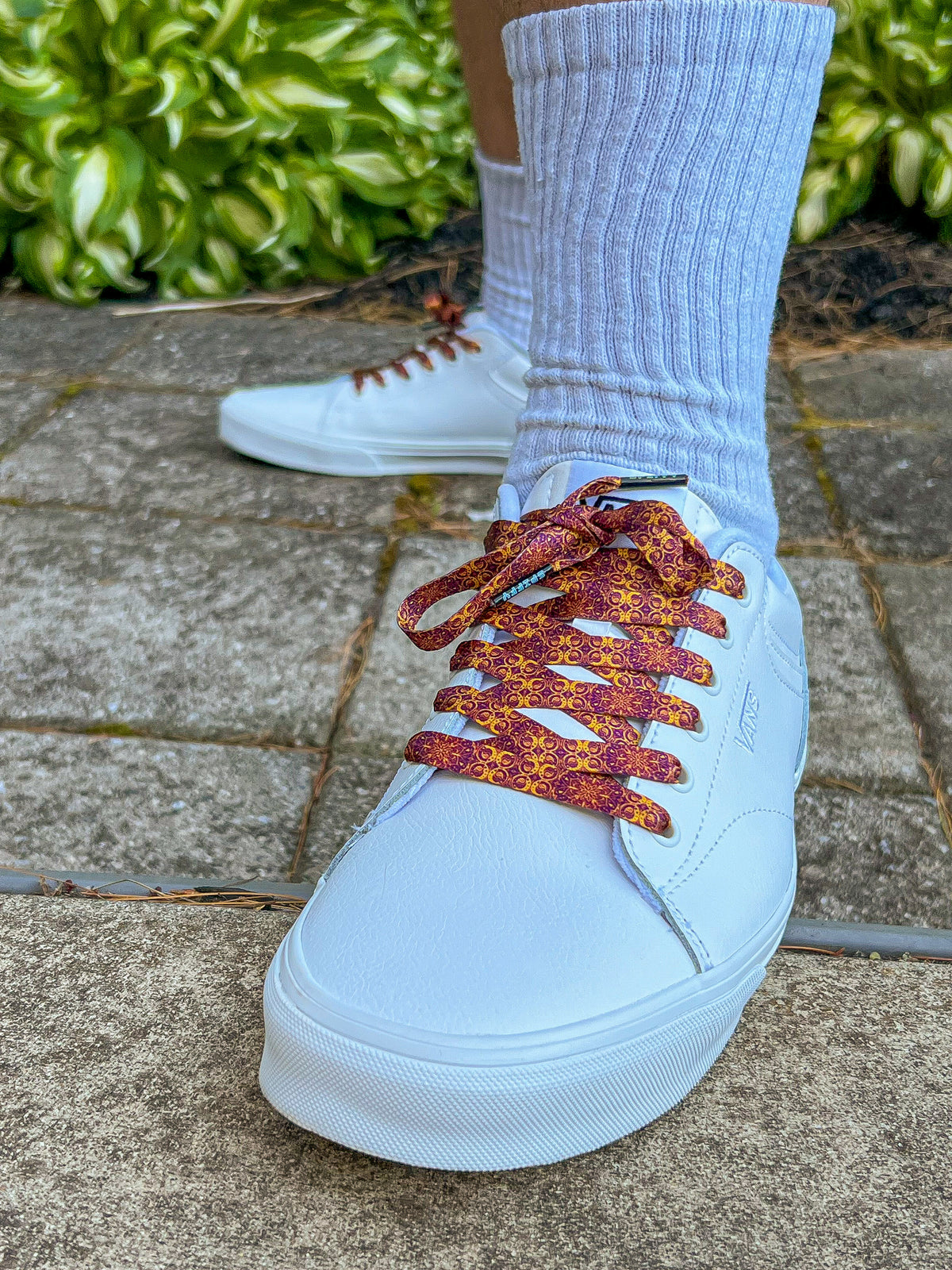 White sneakers with orange and red patterned laces on a concrete surface.