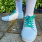 White sneakers with blue laces worn on a concrete surface with greenery in the background
