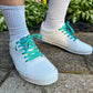 White sneakers with blue laces worn on a concrete surface with greenery in the background