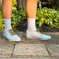 White sneakers with colorful laces worn on a concrete surface with greenery in the background