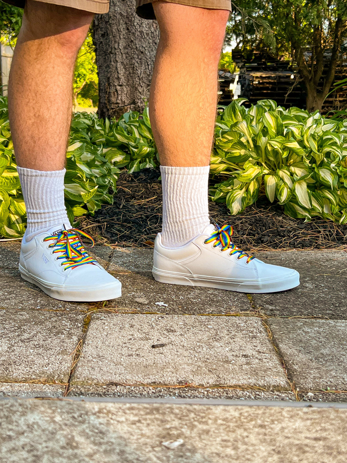 White sneakers with colorful laces worn on a concrete surface with greenery in the background