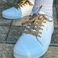 Light blue sneakers with leopard print laces on a stone pavement