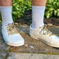White sneakers with  leopard print shoelaces worn on a concrete surface with greenery in the background