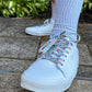 White sneakers with colorful mushroom shoelaces worn on a concrete surface with greenery in the background