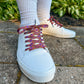 White sneakers with colorful laces worn on a stone surface with green plants in the background