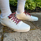 White sneakers with colorful laces worn on a concrete surface with greenery in the background