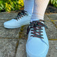 White sneakers with black and red laces worn on a concrete surface with greenery in the background.