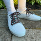 White sneakers with black and red laces worn on a concrete surface with greenery in the background