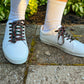 White sneakers with rose shoelaces worn on a concrete surface with grass in the background