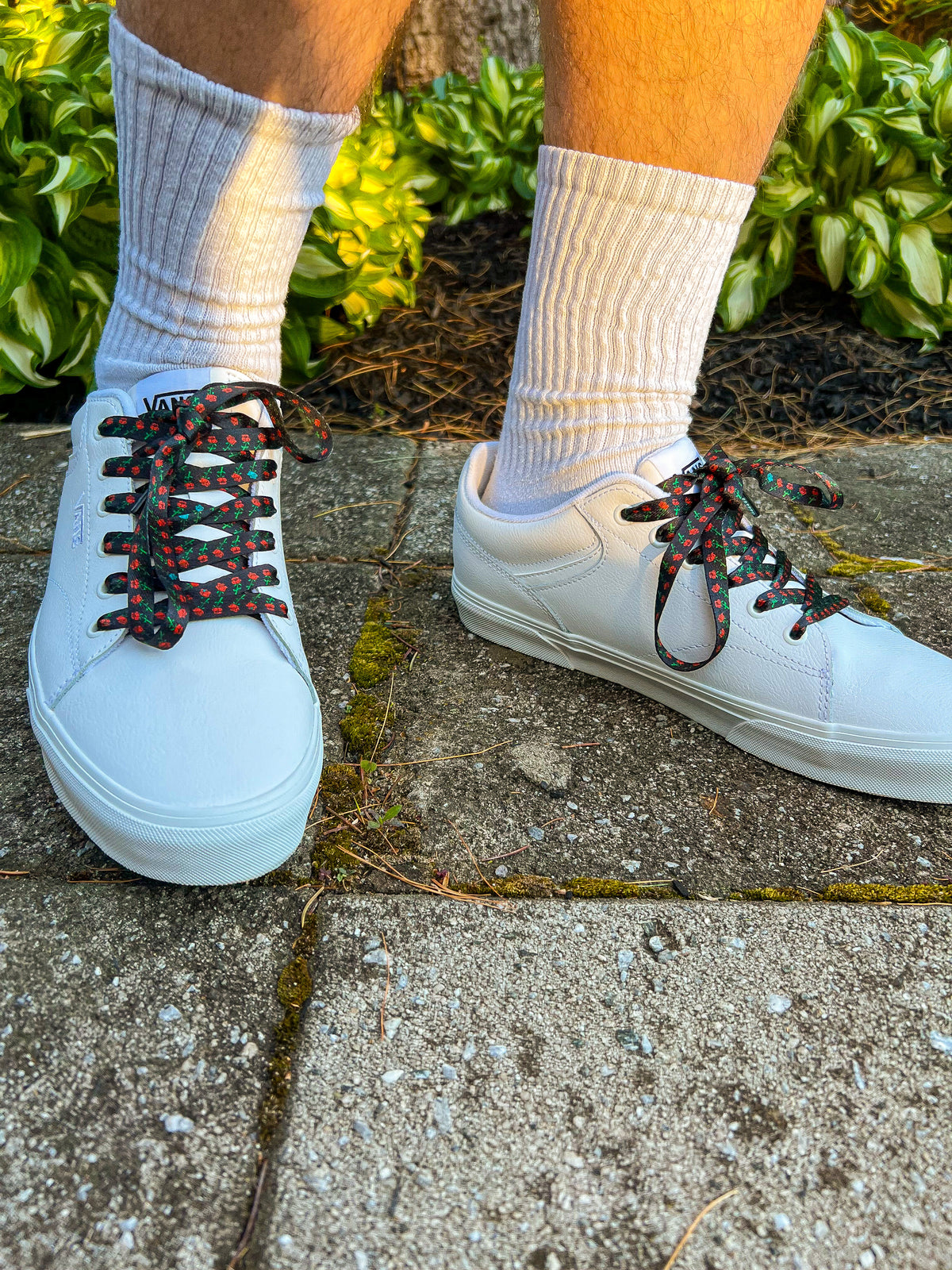 White sneakers with rose shoelaces worn on a concrete surface with grass in the background