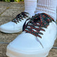 White sneakers with black and red rose patterned laces worn on a concrete surface.