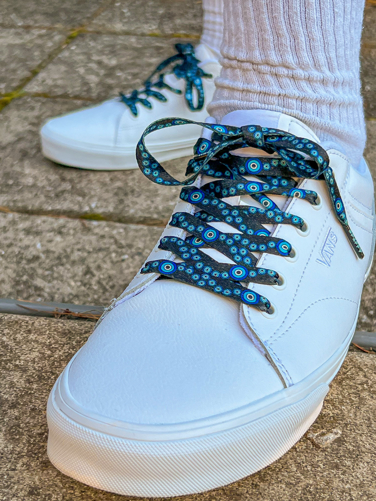White sneakers with blue and black patterned laces on a concrete surface
