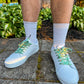 White sneakers with zombie themed laces worn by a person on a stone path with plants in the background