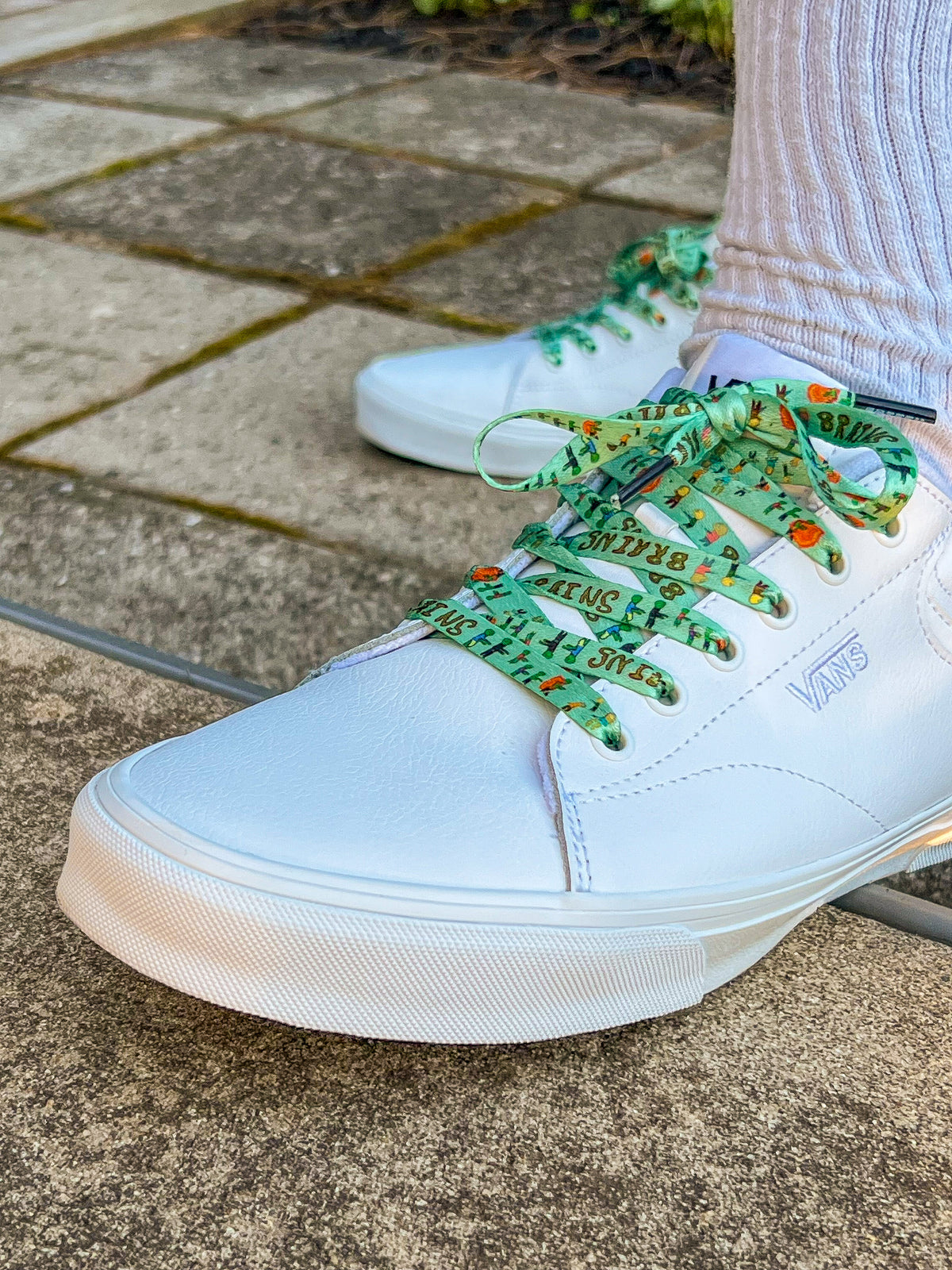 White sneakers with green laces on a concrete surface