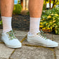 White sneakers with decorative laces worn outdoors on a paved surface.