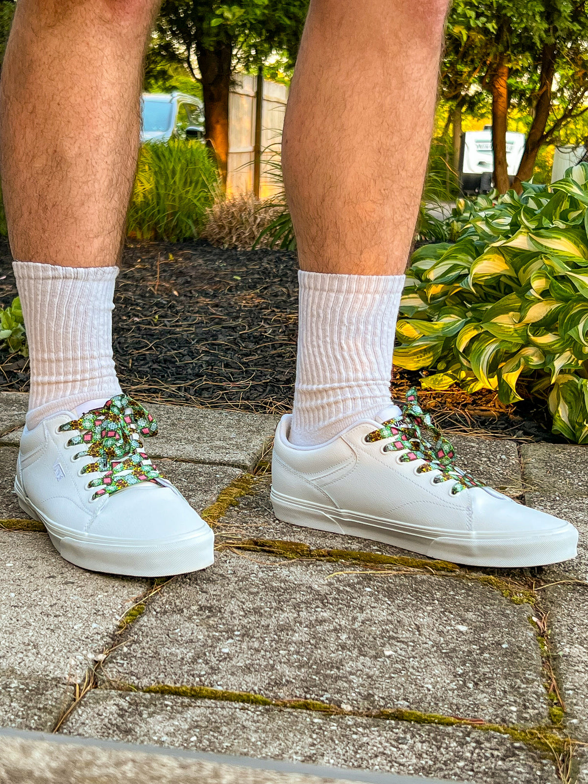 White sneakers with decorative laces worn outdoors on a paved surface.
