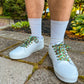 White sneakers with colorful laces worn on a concrete surface with greenery in the background