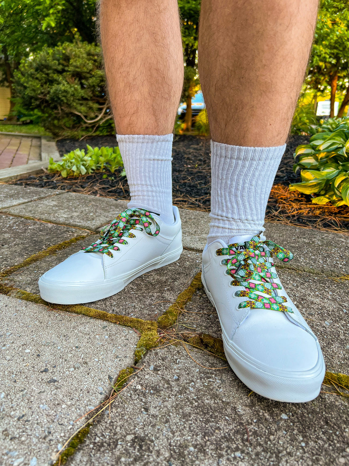White sneakers with colorful laces worn on a concrete surface with greenery in the background