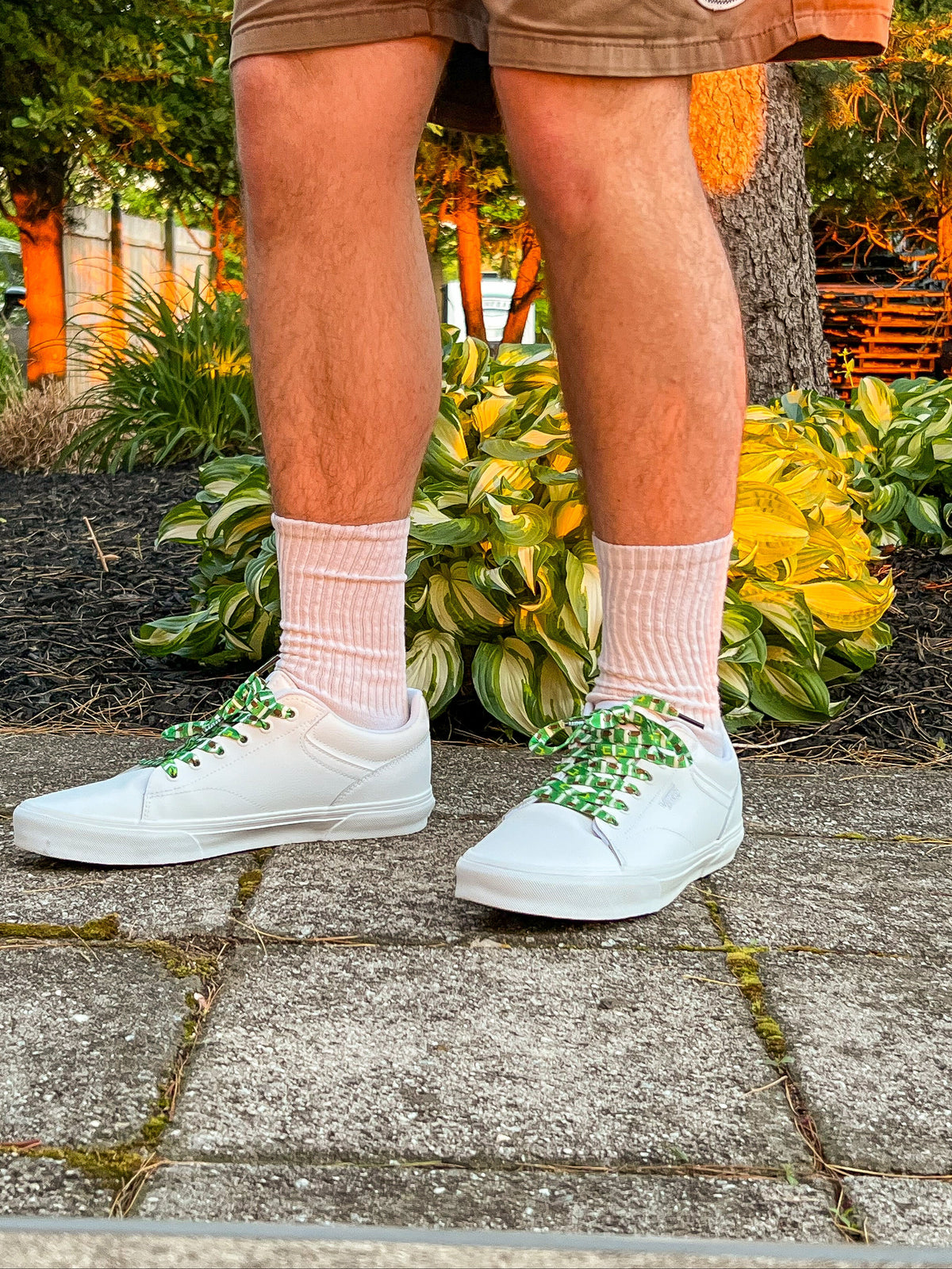 Person wearing white sneakers with colorful football themed shoelaces, pink socks, and brown shorts.