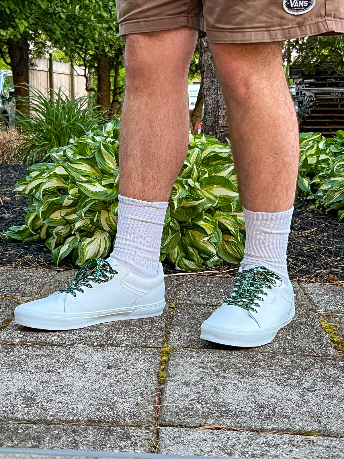 Person wearing white sneakers with cow shoelaces  on a concrete surface with plants in the background