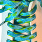 Close-up of blue and green frog shoelaces on a white sneaker with a light pink heel.