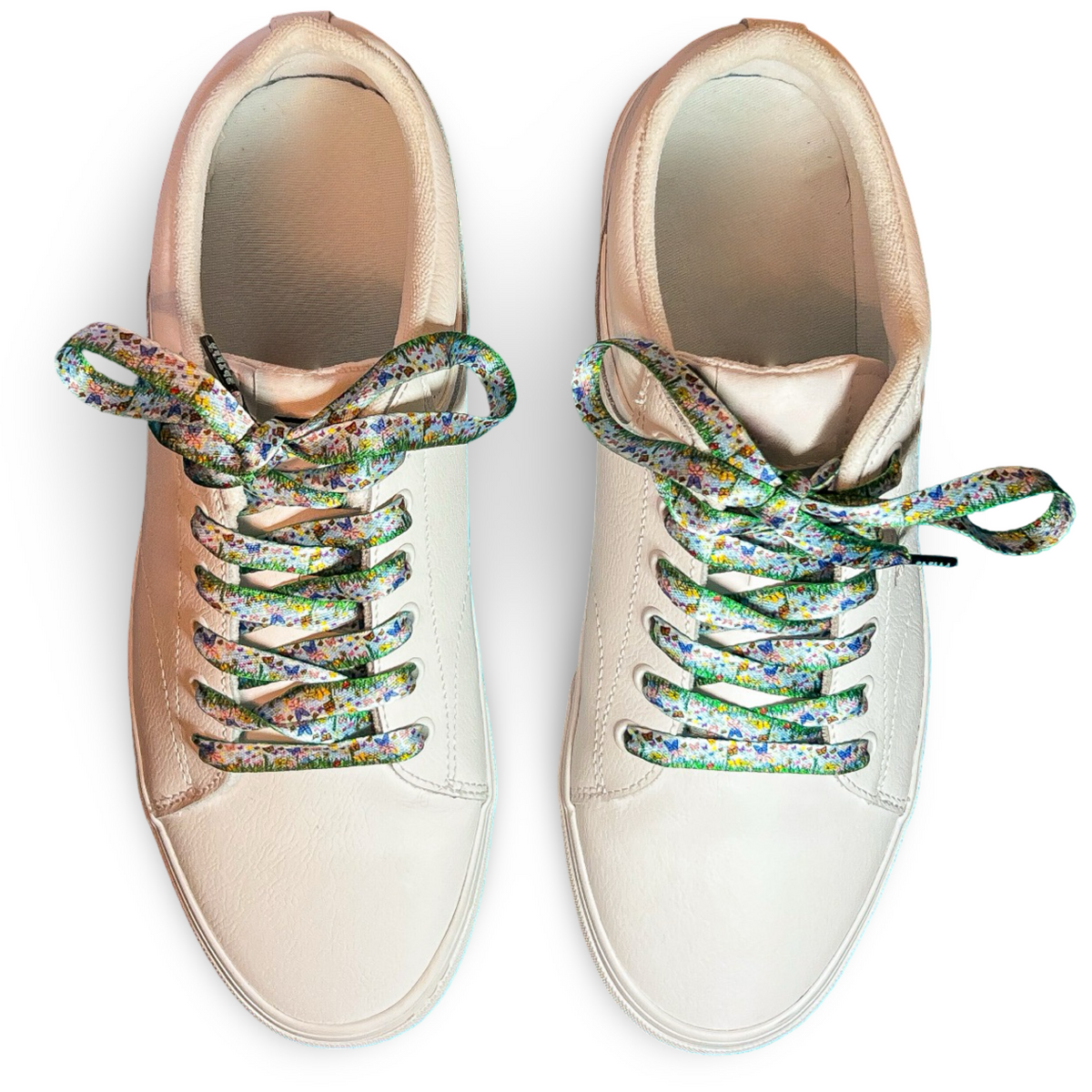 Pair of white sneakers with colorful butterfly themed laces on a white background