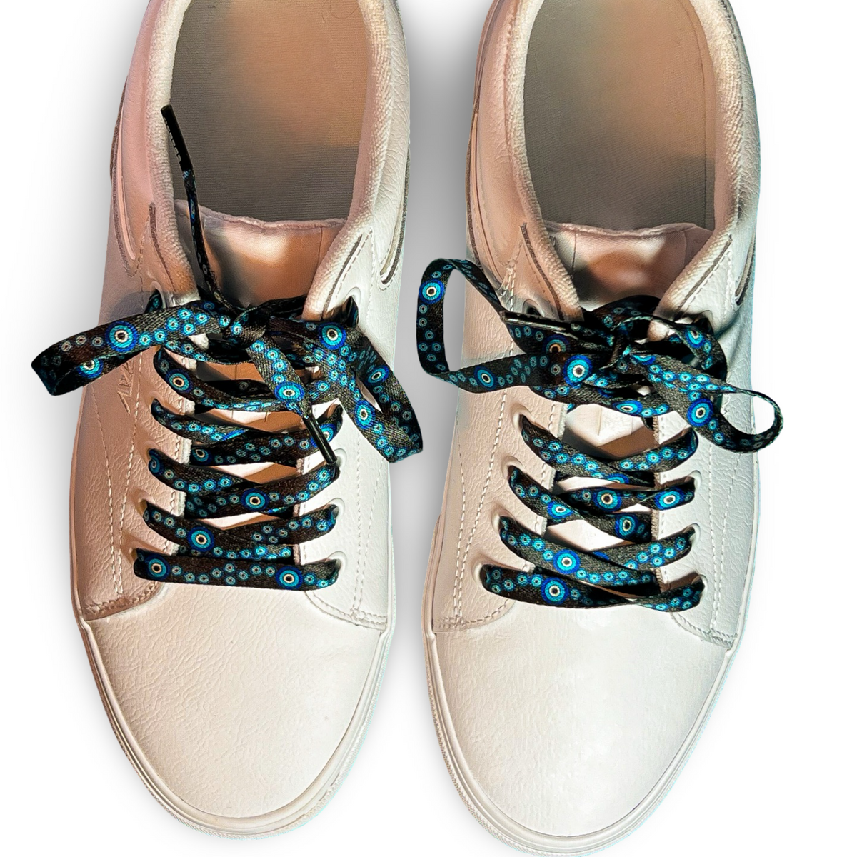 Pair of white sneakers with evil eye themed shoelaces on a white background