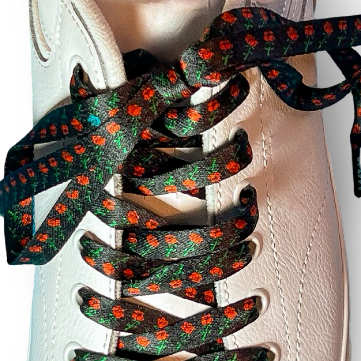 Close-up of a white shoe with rose printed shoelaces on a light background