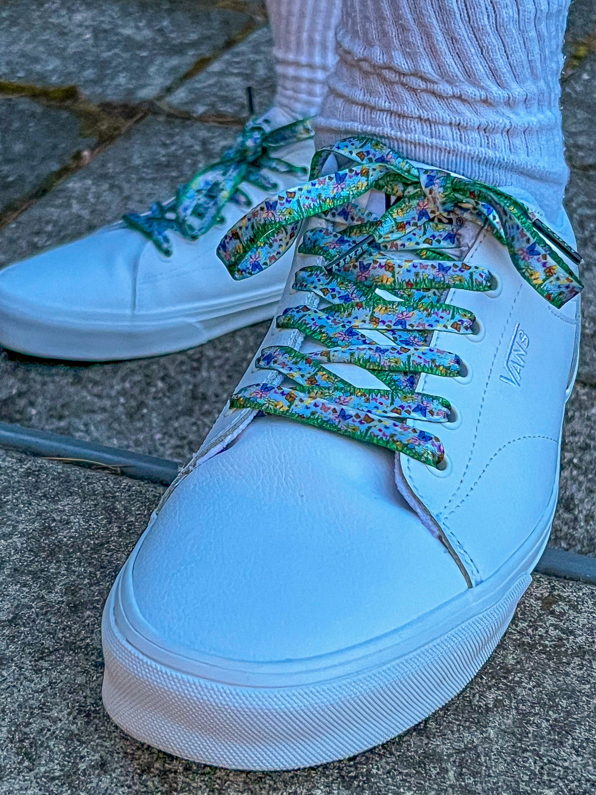 White sneakers with colorful butterfly themed laces on a concrete surface