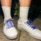White sneakers with blueberry themed laces worn on a concrete surface