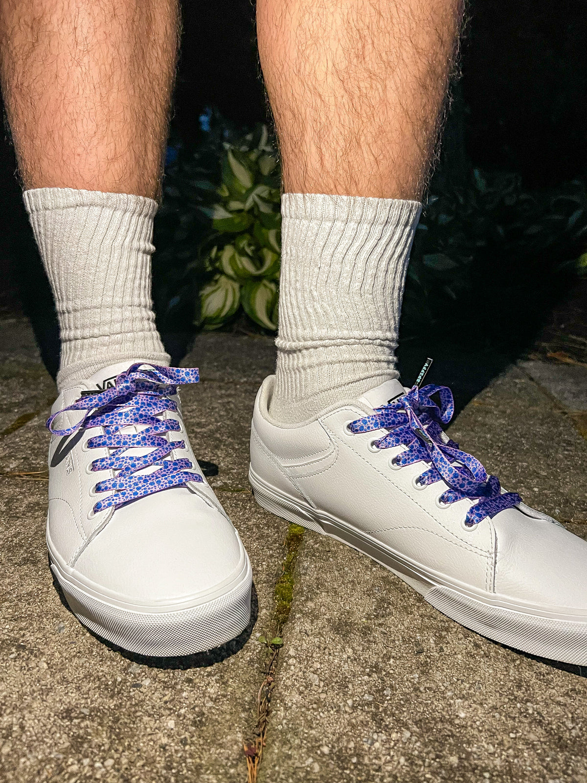 White sneakers with blueberry themed laces worn on a concrete surface